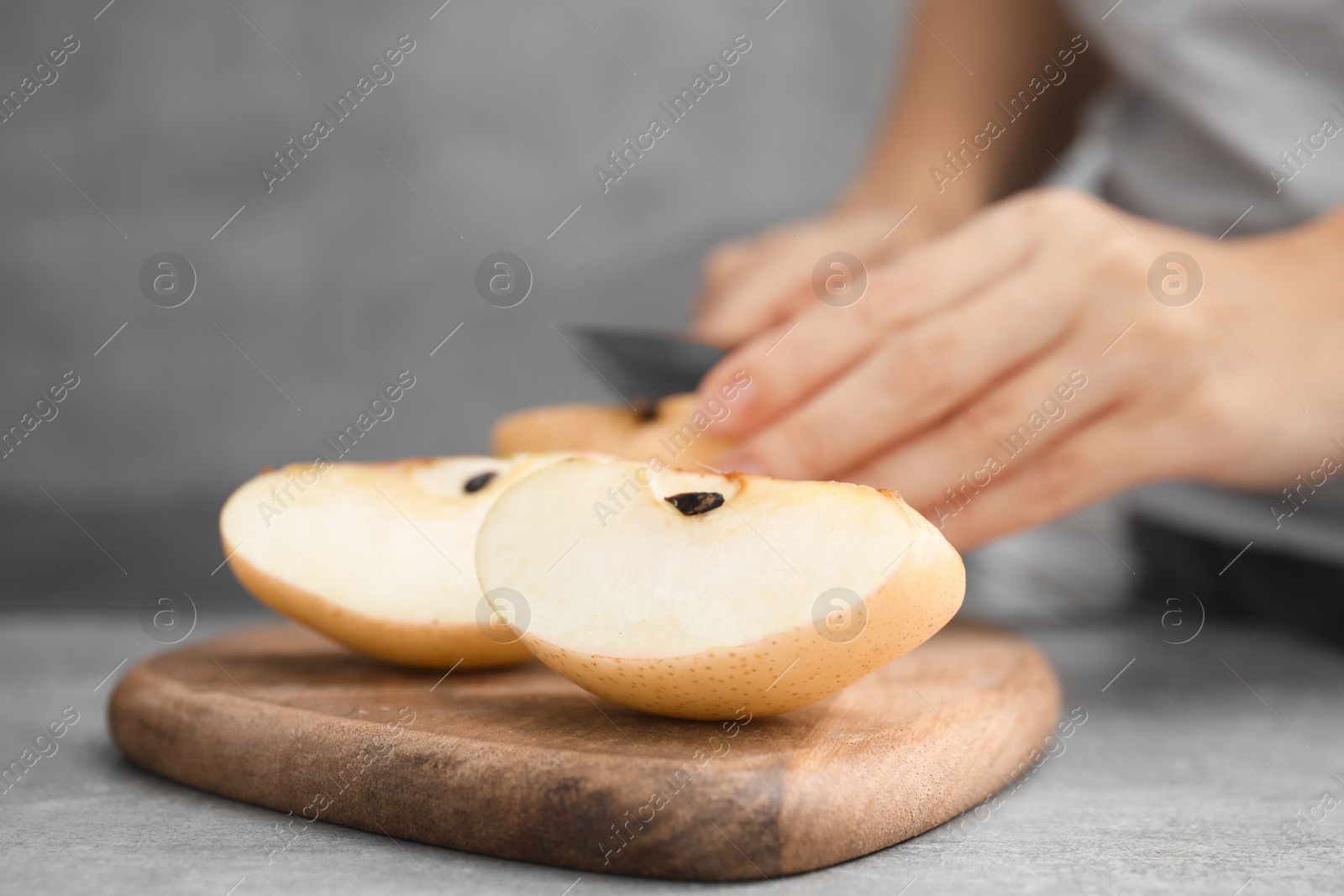 Photo of Woman cutting fresh apple pear at grey table, focus on fruit