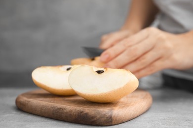 Photo of Woman cutting fresh apple pear at grey table, focus on fruit