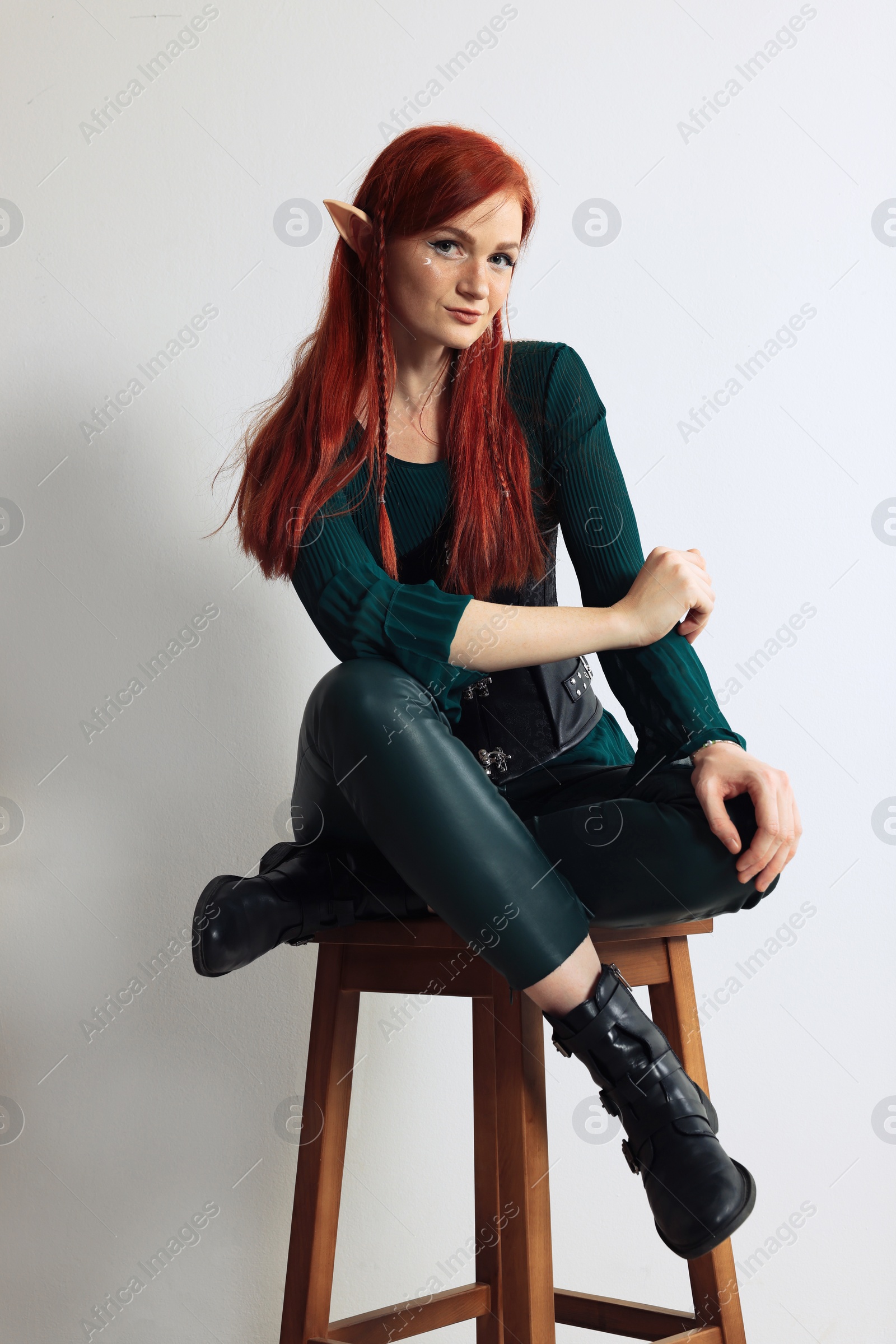 Photo of Beautiful redhead elf girl sitting on stool against light background