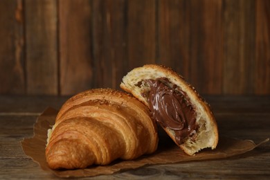 Photo of Tasty croissants with chocolate and sesame seeds on wooden table