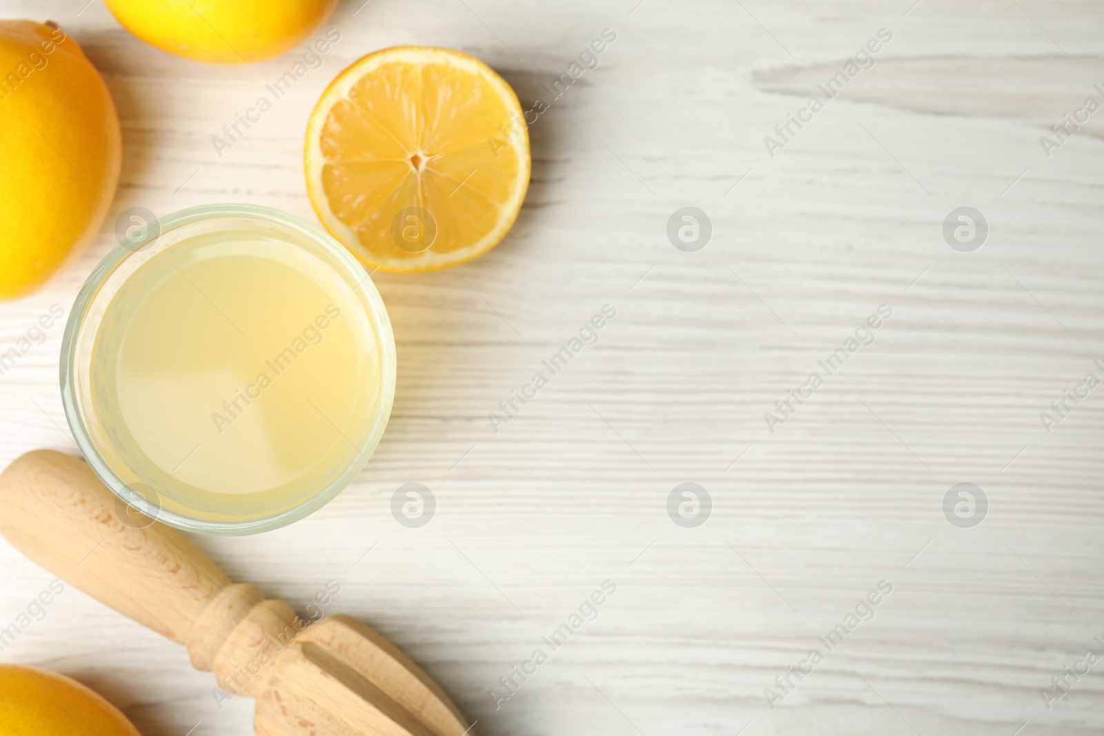 Photo of Freshly squeezed juice, lemons and reamer on white wooden table, flat lay. Space for text