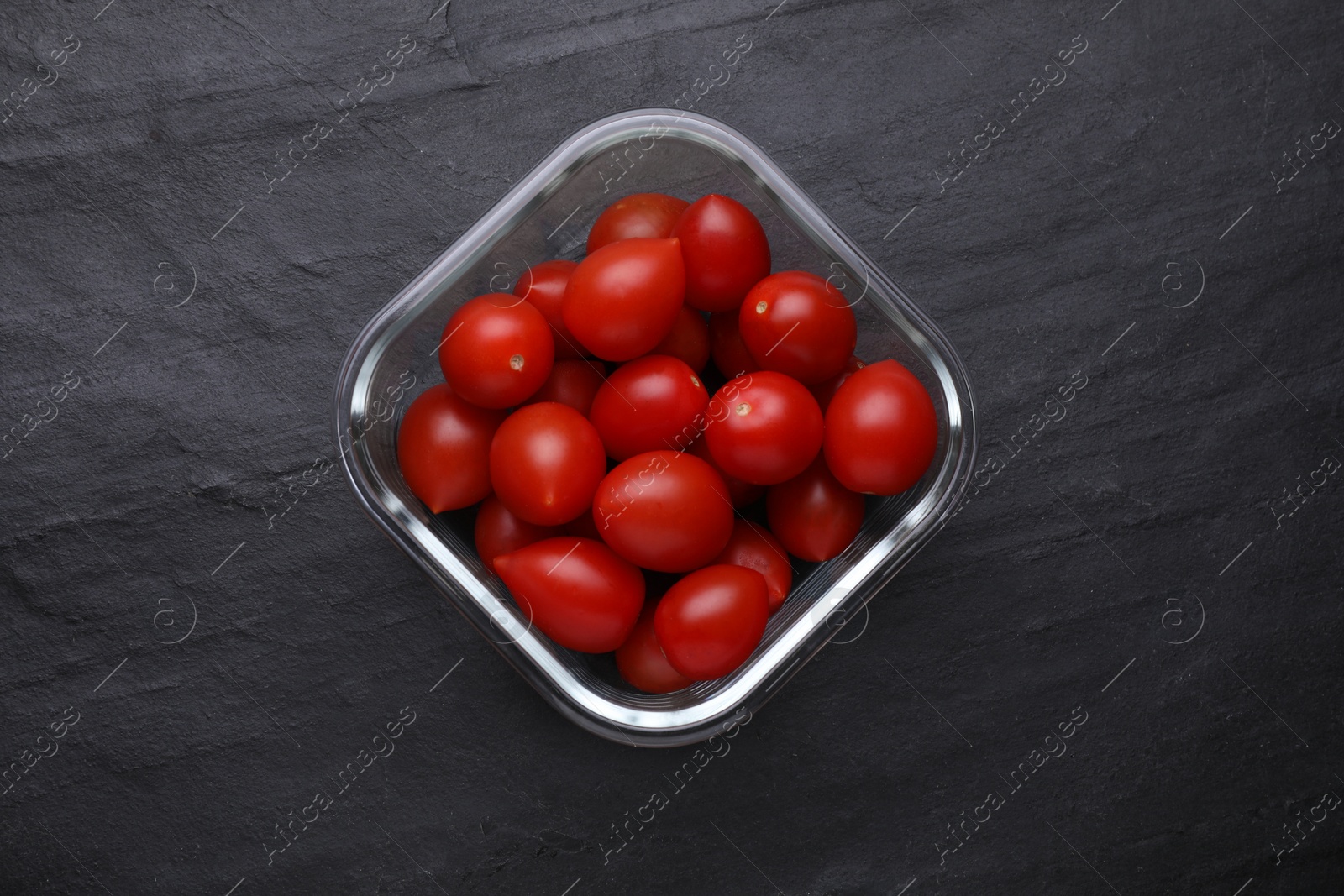 Photo of Glass container with fresh cherry tomatoes on black table, top view