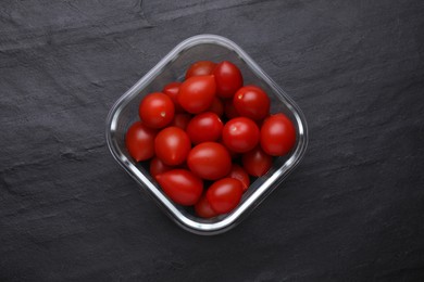 Glass container with fresh cherry tomatoes on black table, top view