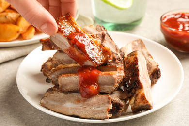 Woman with grilled ribs at light grey table, closeup