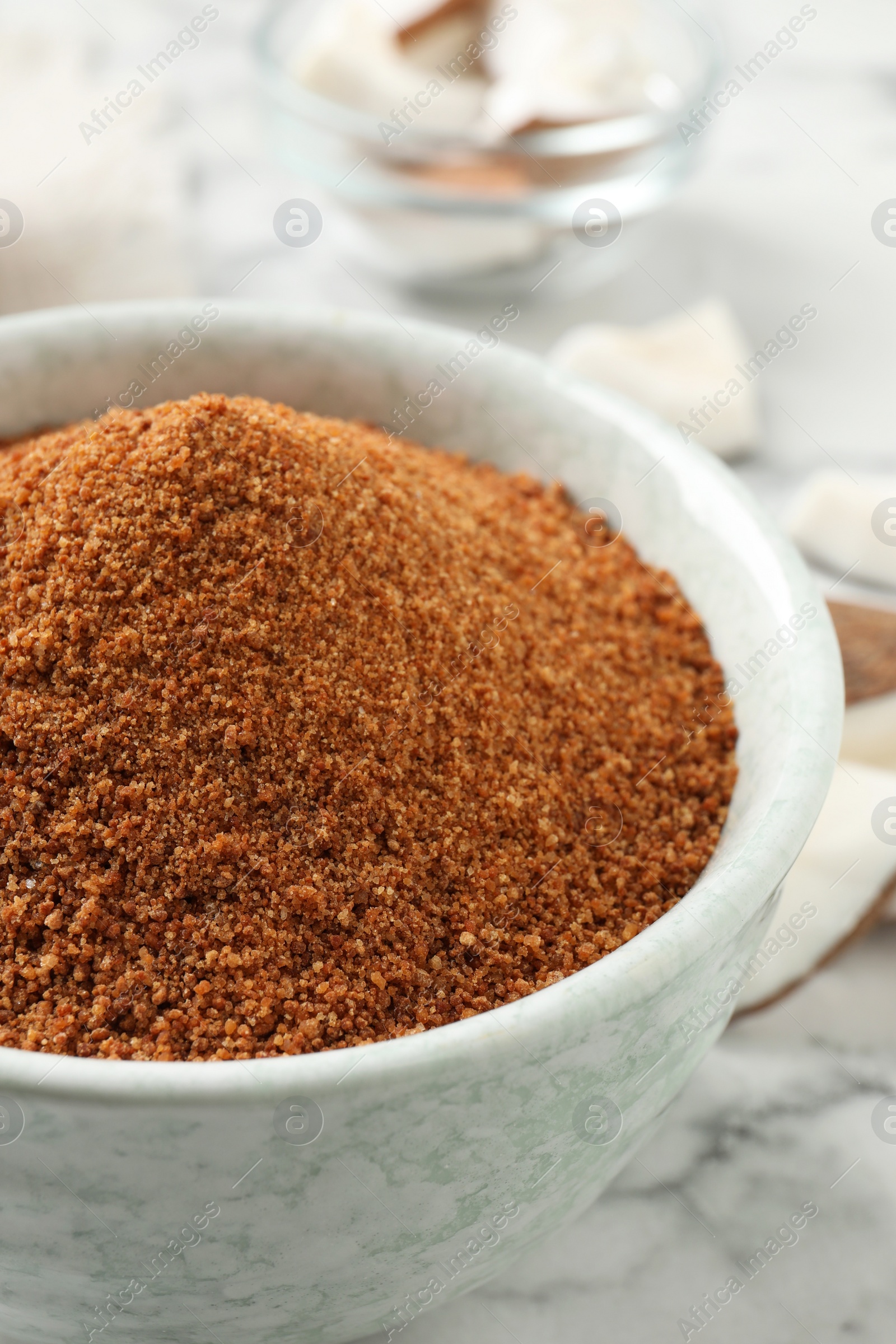 Photo of Natural coconut sugar in ceramic bowl on white marble table, closeup