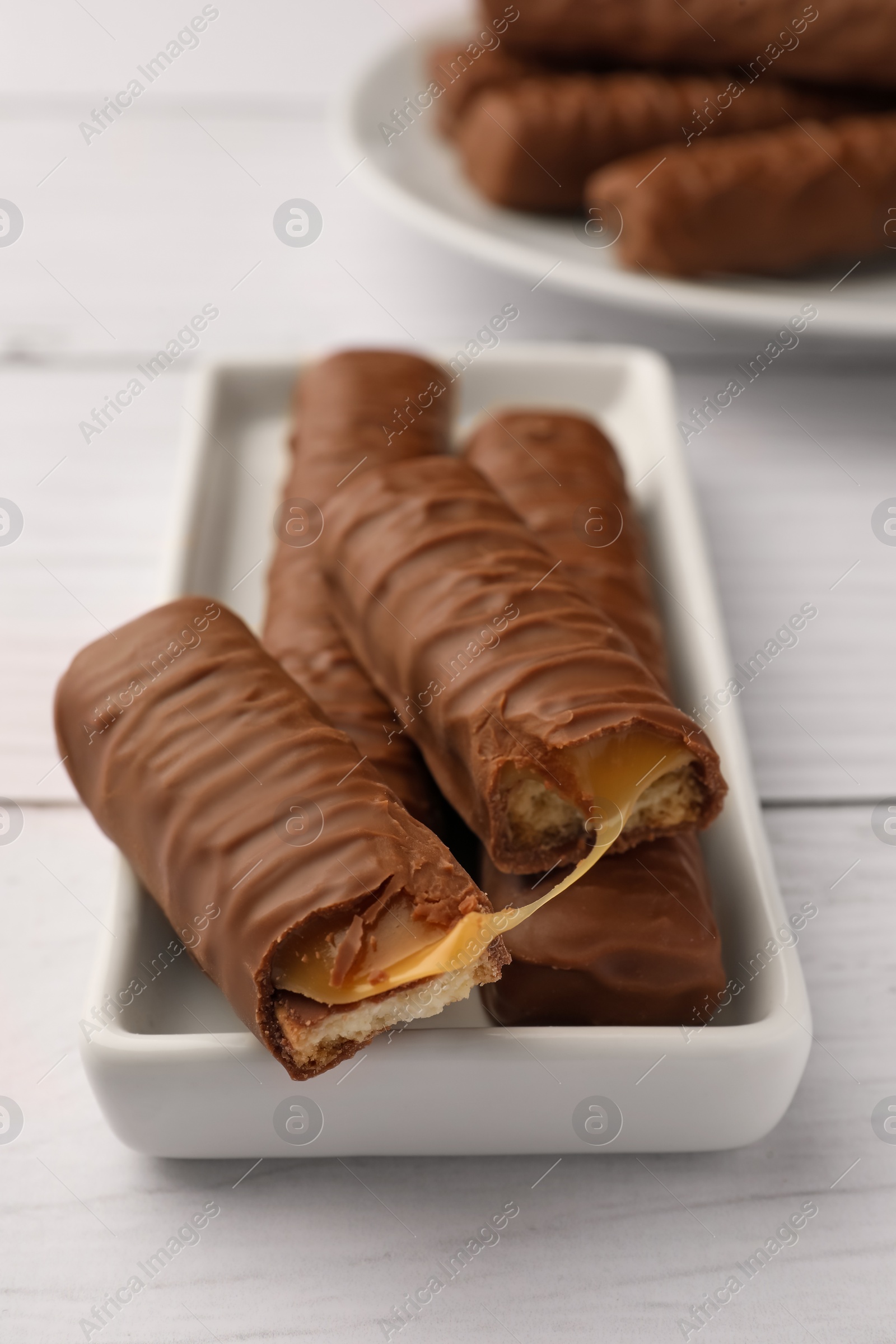 Photo of Tasty chocolate bars with caramel on white wooden table, closeup