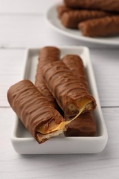 Tasty chocolate bars with caramel on white wooden table, closeup