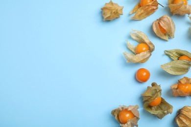 Ripe physalis fruits with dry husk on light blue background, flat lay. Space for text