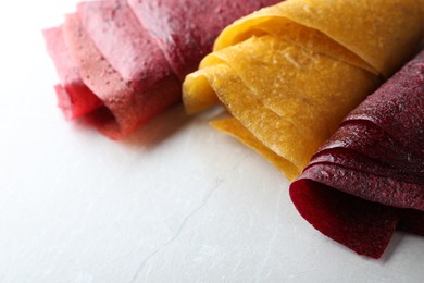 Photo of Delicious fruit leather rolls on light table, closeup