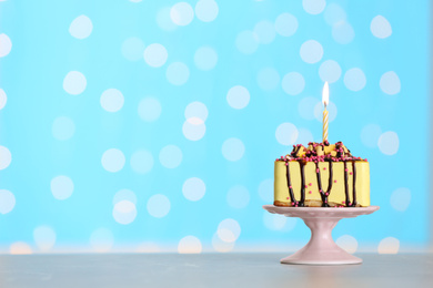 Piece of delicious birthday cake with burning candle on table against festive lights. Space for text