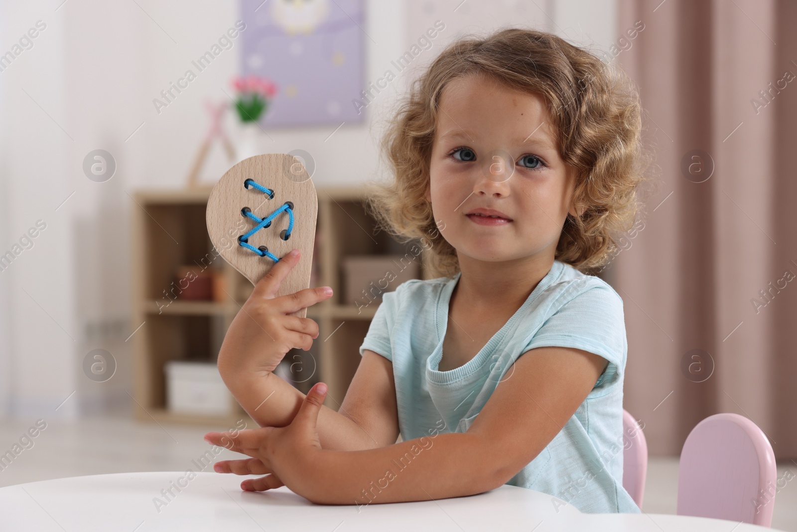 Photo of Motor skills development. Little girl playing with wooden lacing toy at table indoors