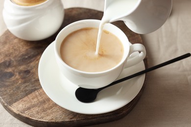 Photo of Pouring milk into cup with tea on light table, closeup