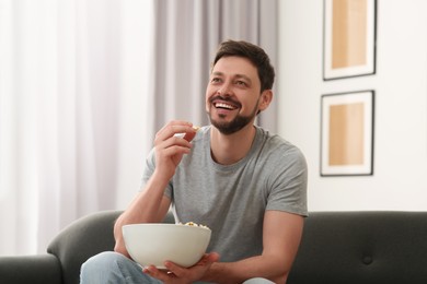 Photo of Happy man with bowlpopcorn watching movie via TV on sofa at home