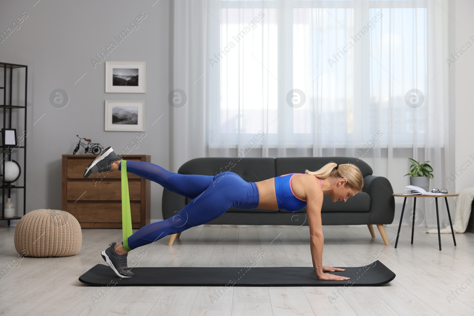 Photo of Athletic woman doing exercise with fitness elastic band on mat at home