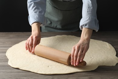 Photo of Woman rolling raw dough at wooden table, closeup