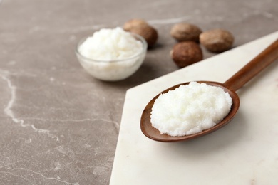 Photo of Shea butter in wooden spoon and bowl with nuts on grey background