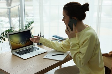 Photo of Woman talking on phone while working with laptop in office. Forex trading