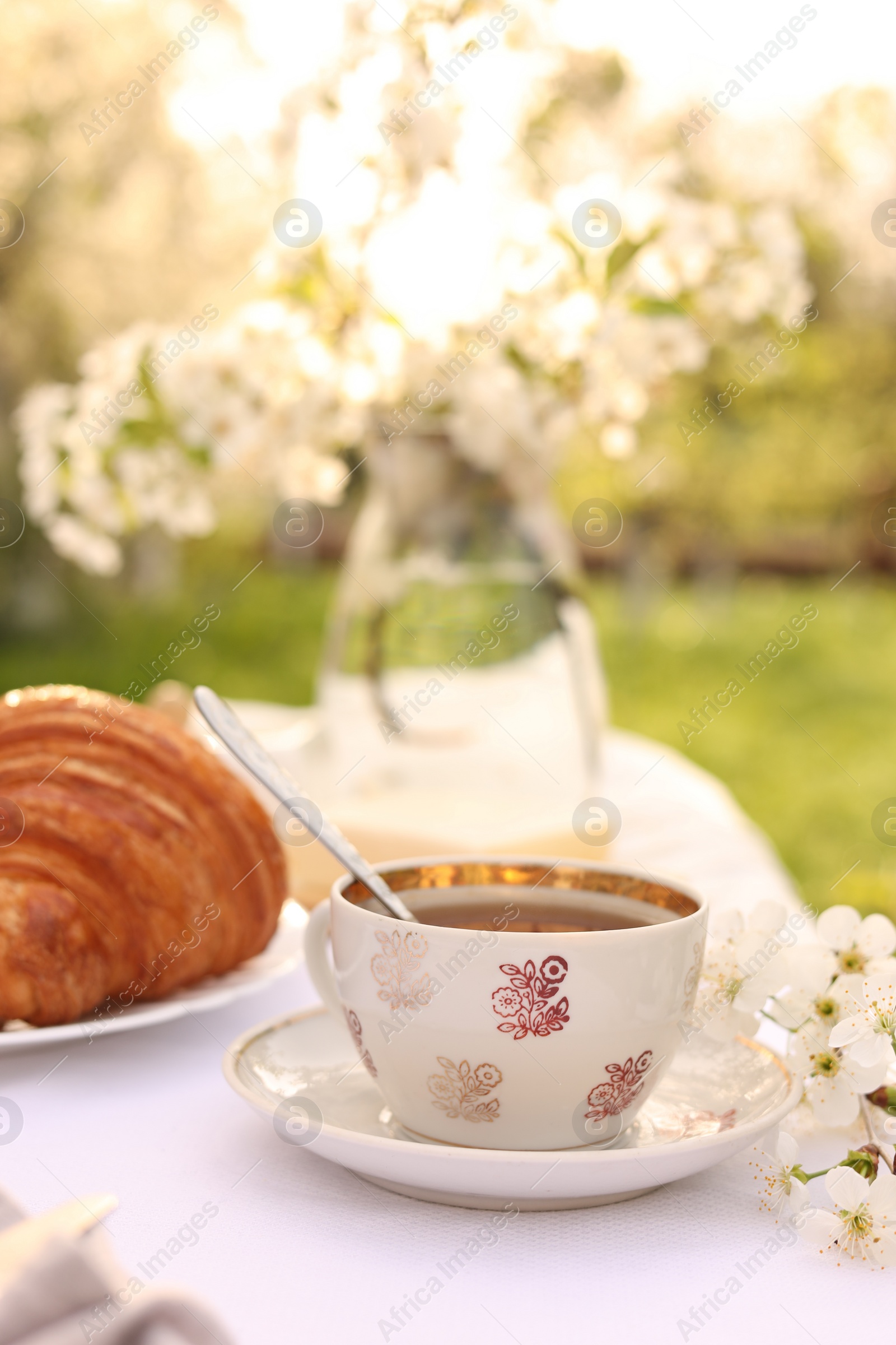 Photo of Stylish table setting with beautiful spring flowers, tea and croissants in garden