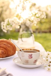 Photo of Stylish table setting with beautiful spring flowers, tea and croissants in garden