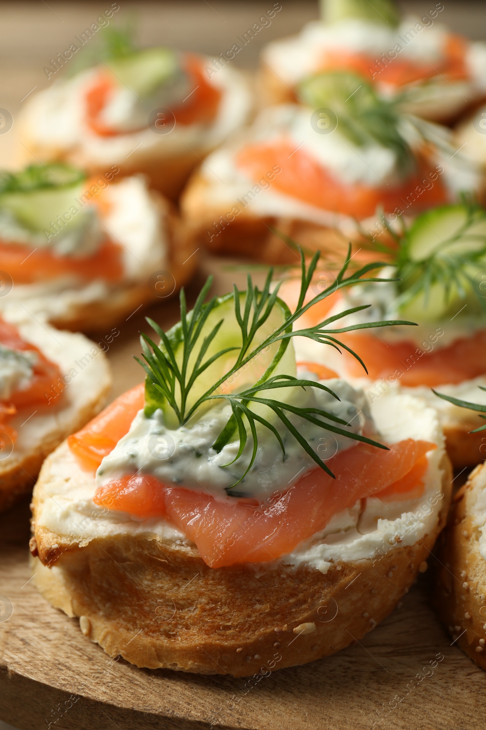 Photo of Tasty canapes with salmon, cucumber, cream cheese and dill on wooden stand, closeup