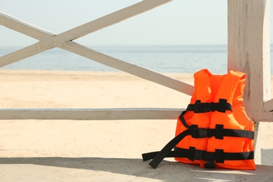 Photo of Orange life jacket near wooden railing on beach  Emergency rescue equipment