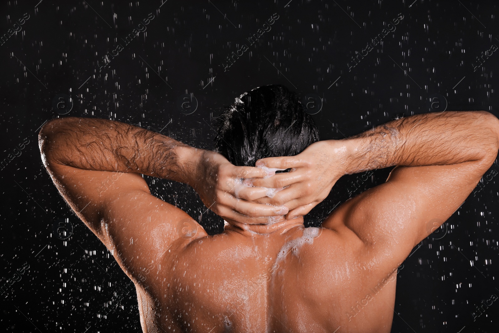 Photo of Man washing hair while taking shower on black background