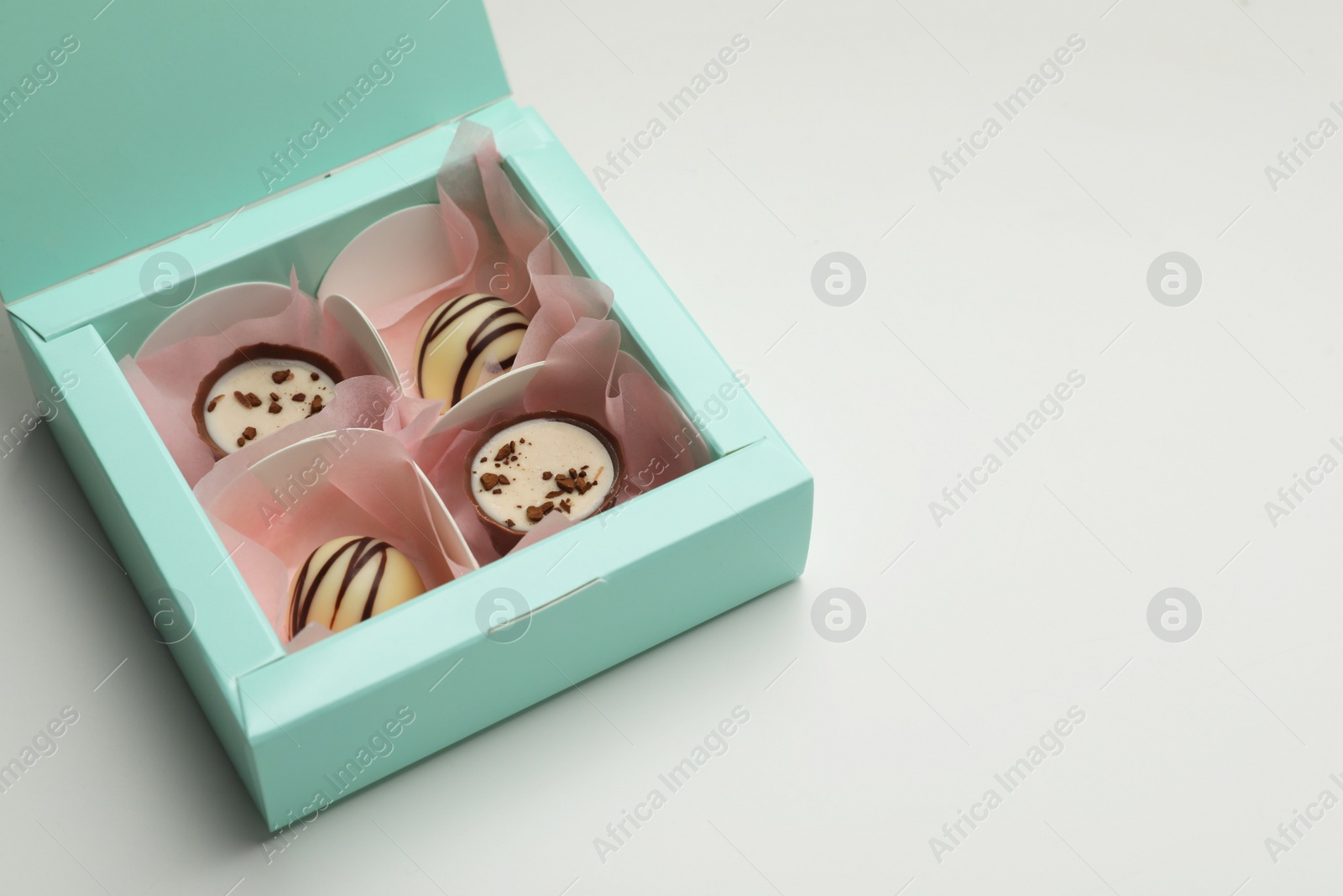 Photo of Delicious chocolate candies in turquoise box on light grey background, space for text