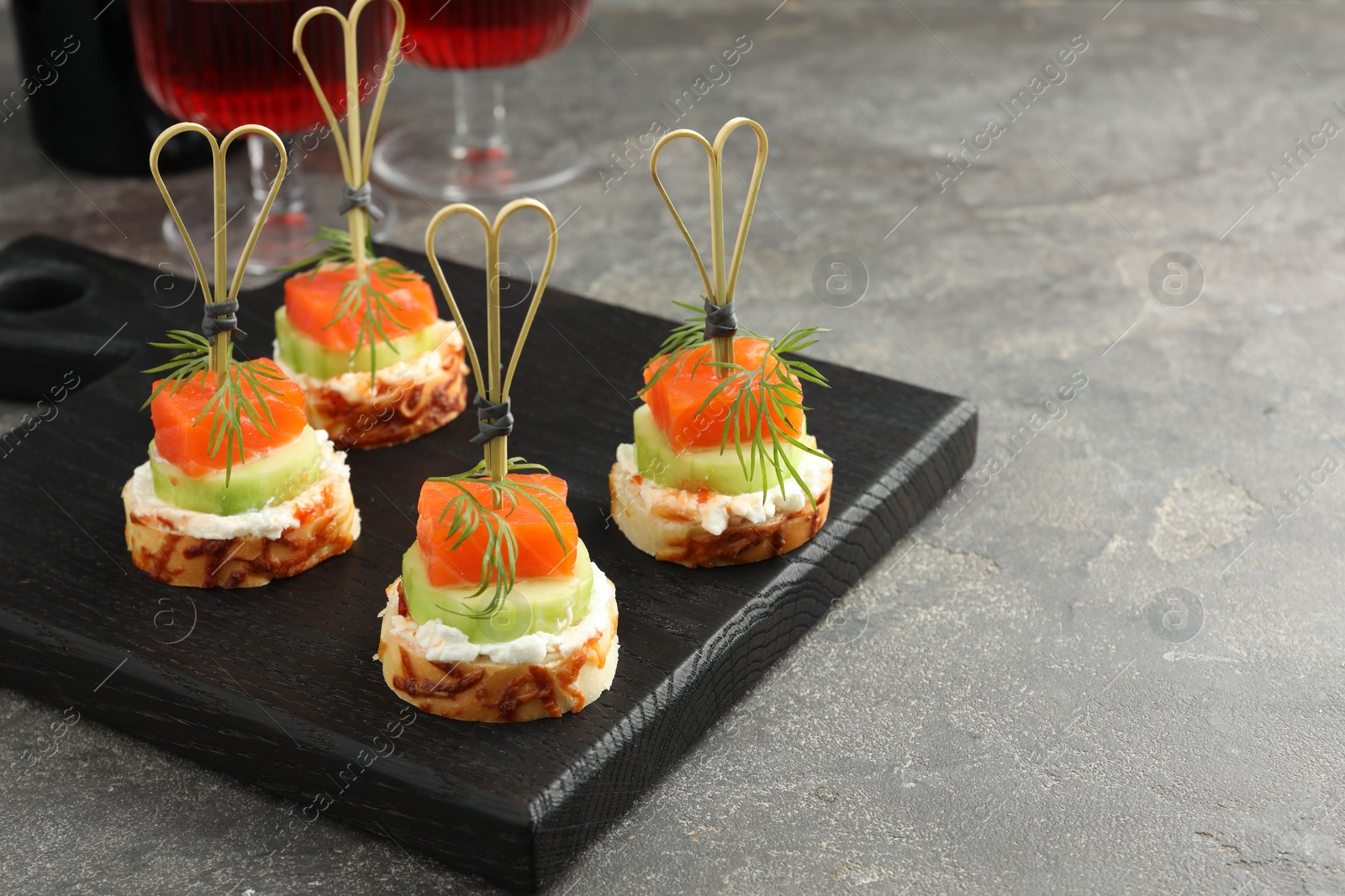 Photo of Tasty canapes with salmon, cucumber, bread and cream cheese on grey table