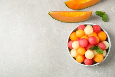 Photo of Melon balls and mint in bowl on grey table, flat lay. Space for text