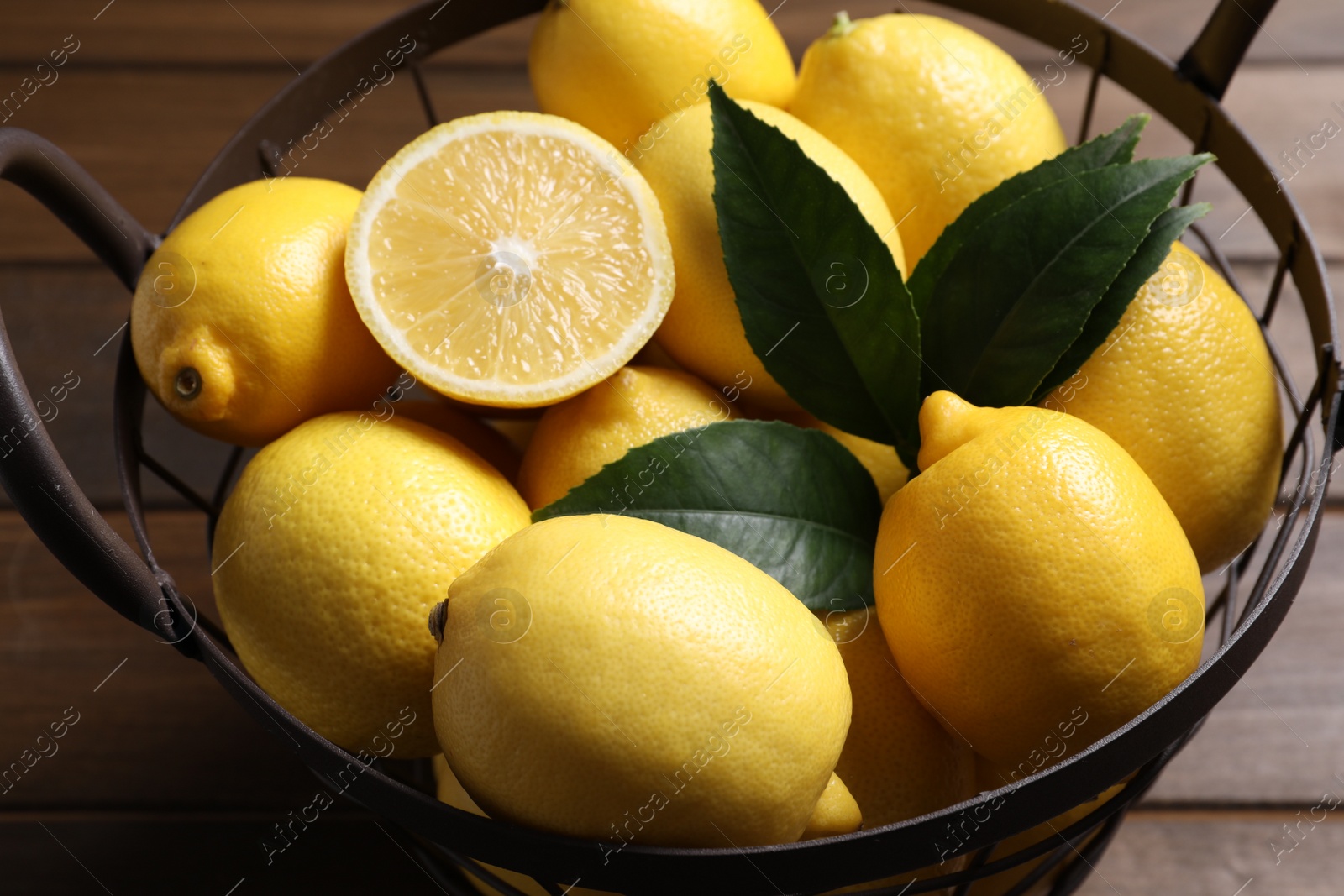 Photo of Many fresh ripe lemons with green leaves on wooden table, closeup