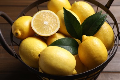Many fresh ripe lemons with green leaves on wooden table, closeup