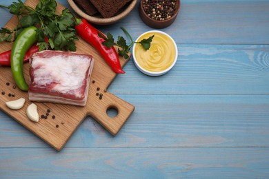 Piece of pork fatback with garlic and chilli pepper on light blue wooden table, flat lay. Space for text