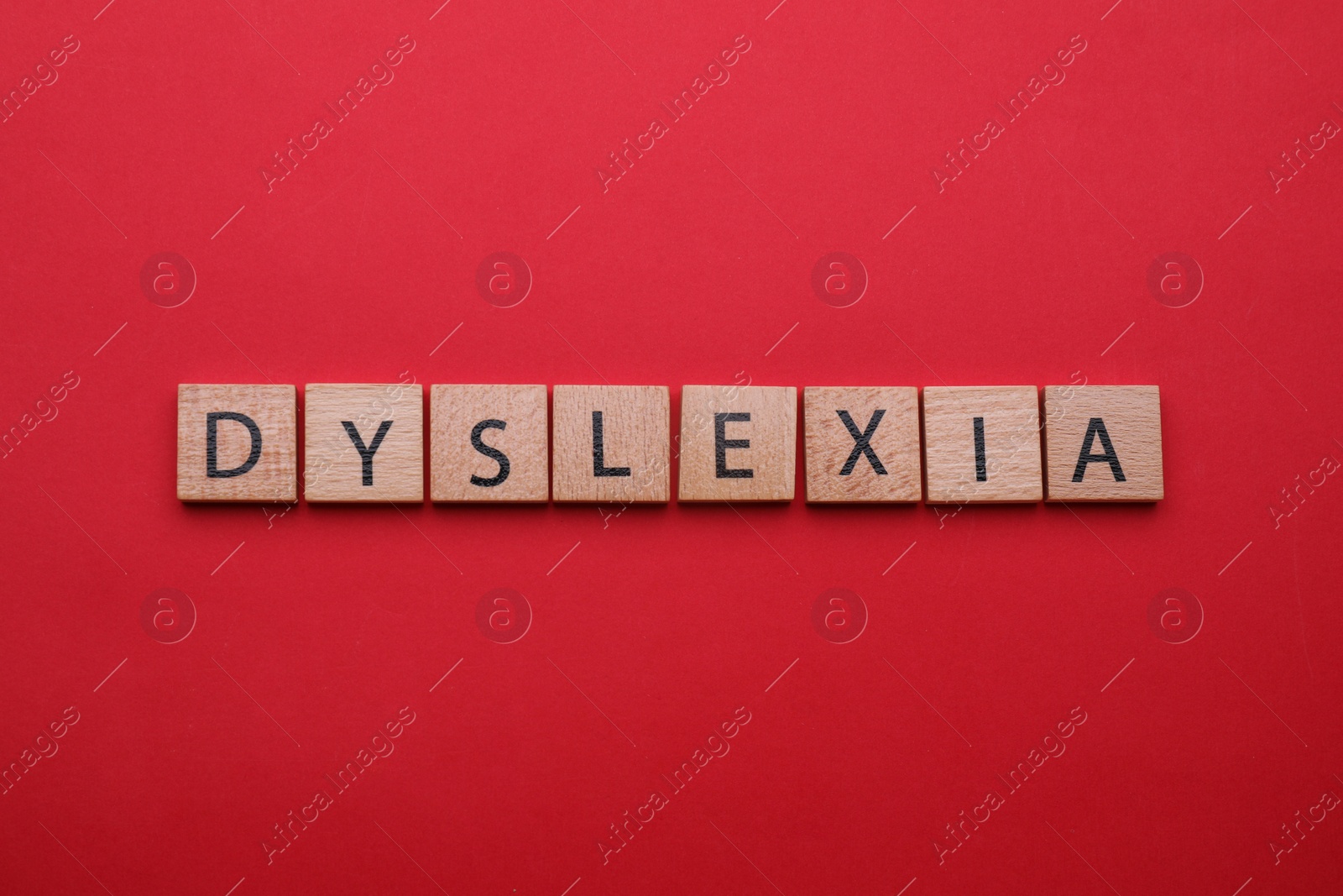 Photo of Wooden tiles with word Dyslexia on red background, flat lay