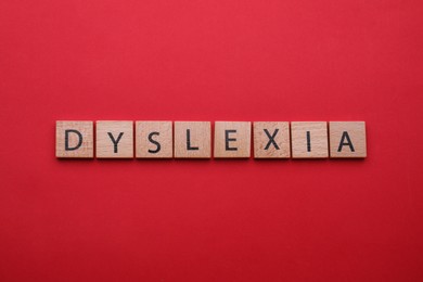 Wooden tiles with word Dyslexia on red background, flat lay