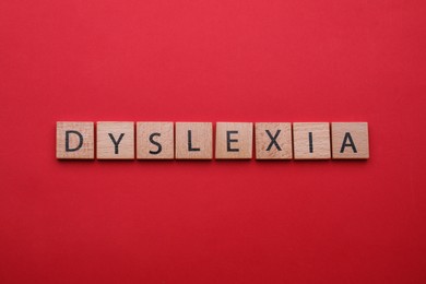 Photo of Wooden tiles with word Dyslexia on red background, flat lay