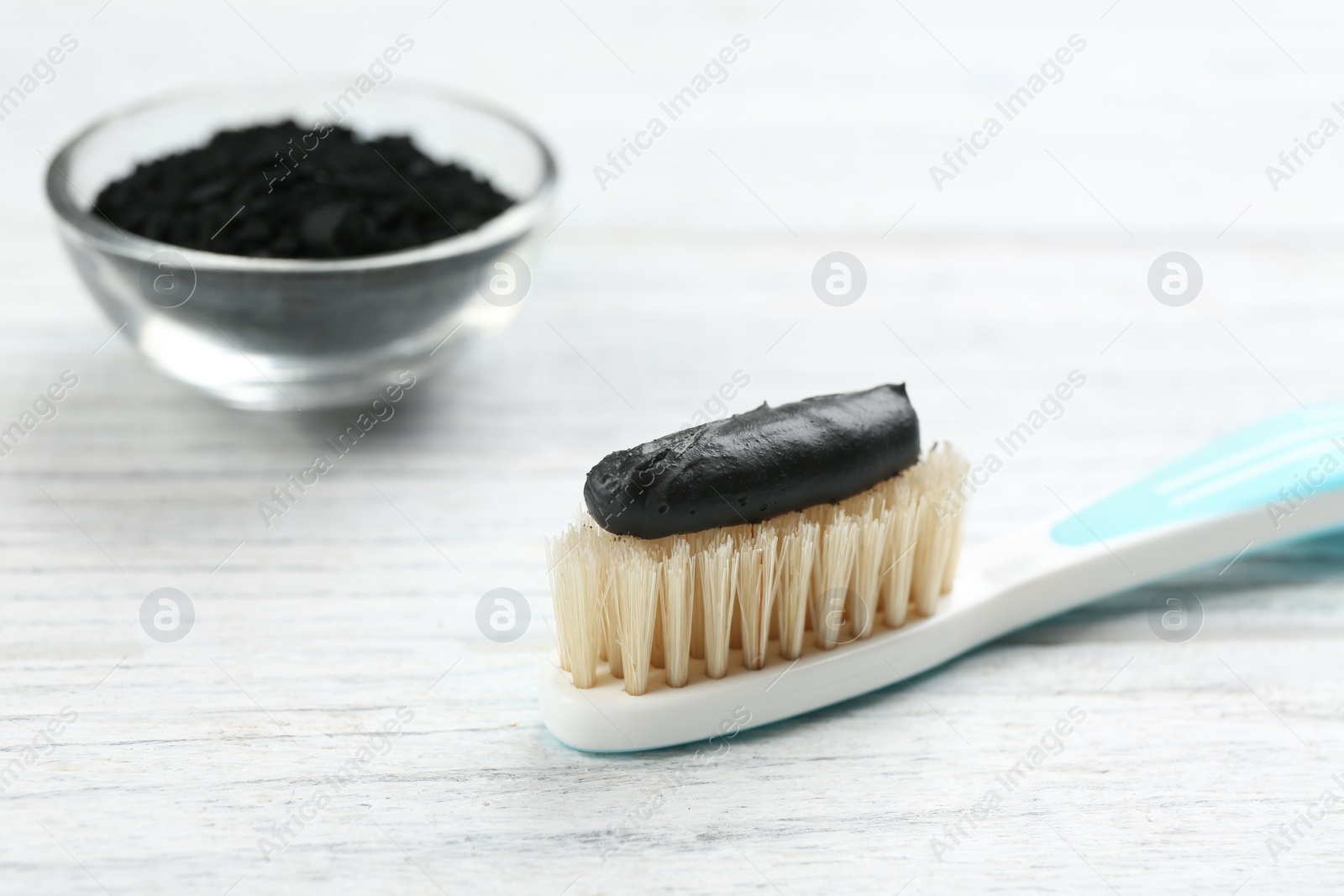 Photo of Toothbrush with natural bristles and charcoal paste on white wooden table, closeup