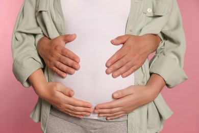 Photo of Man hugging his pregnant wife on pink background, closeup