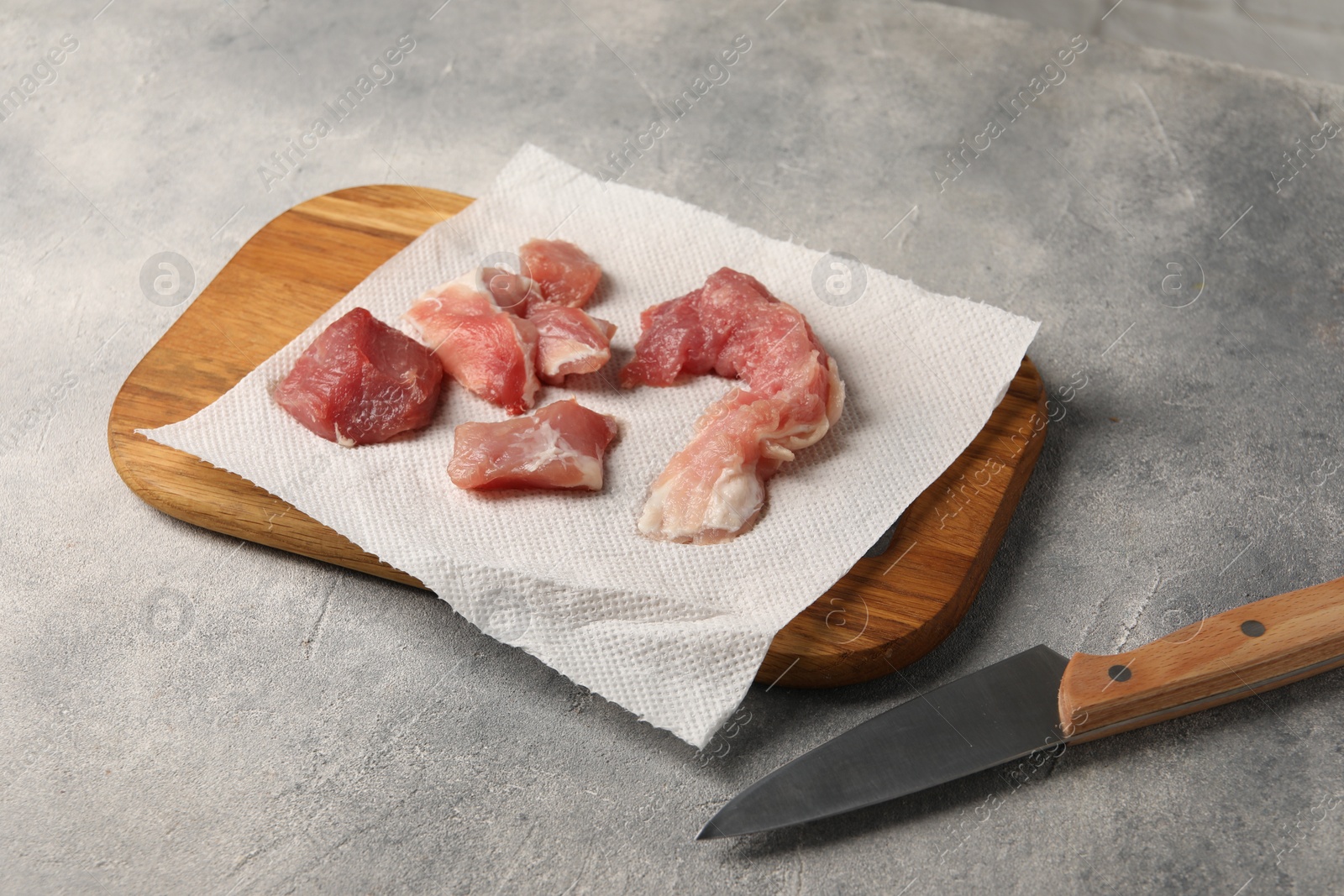 Photo of Paper towel, pieces of meat and knife on grey table