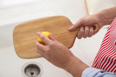 Photo of Man rubbing wooden cutting board with lemon at sink in kitchen, closeup