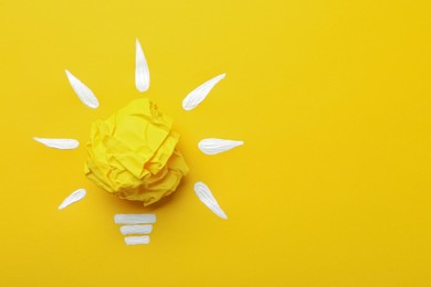 Photo of Composition with crumpled paper ball as lamp bulb on yellow background, top view and space for text. Idea concept