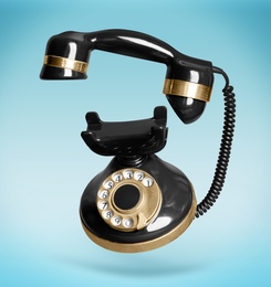 Image of Vintage black corded telephone flying in air on light blue background