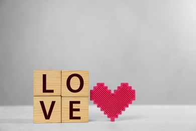 Word Love made of wooden cubes with letters near decorative heart on light table