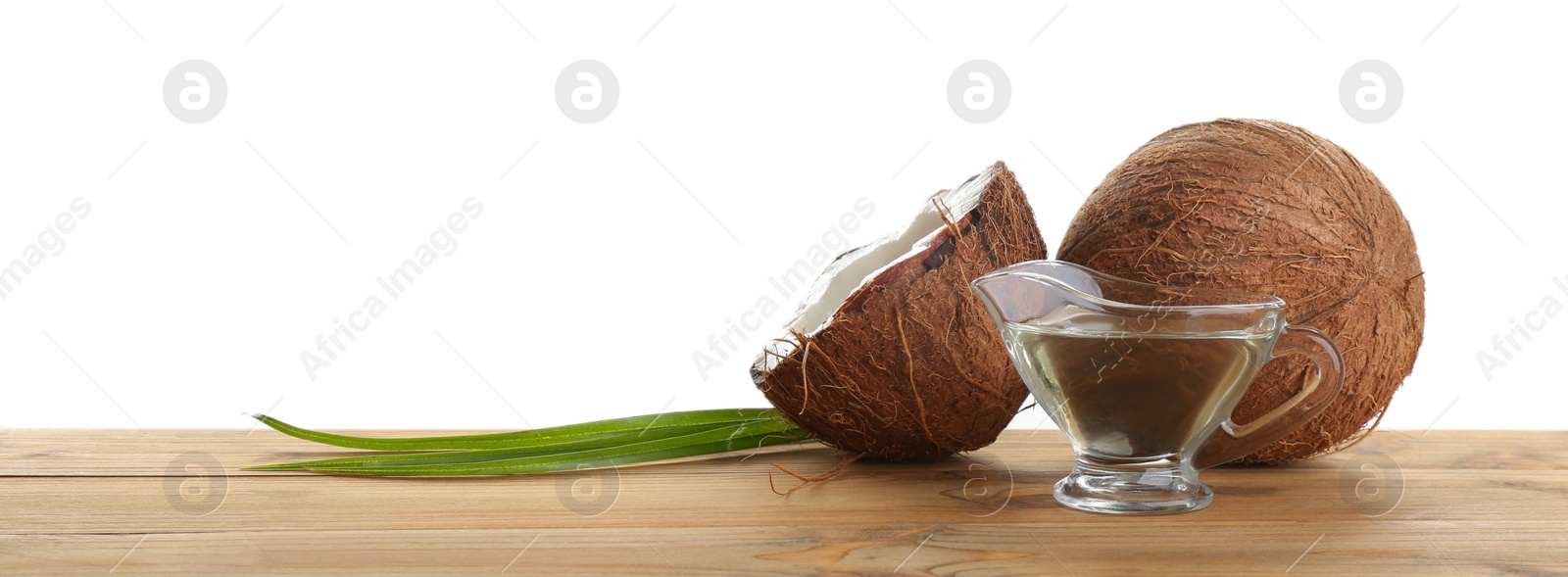 Photo of Ripe coconuts and gravy boat with natural organic oil on wooden table against white background