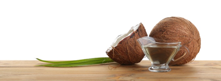 Ripe coconuts and gravy boat with natural organic oil on wooden table against white background