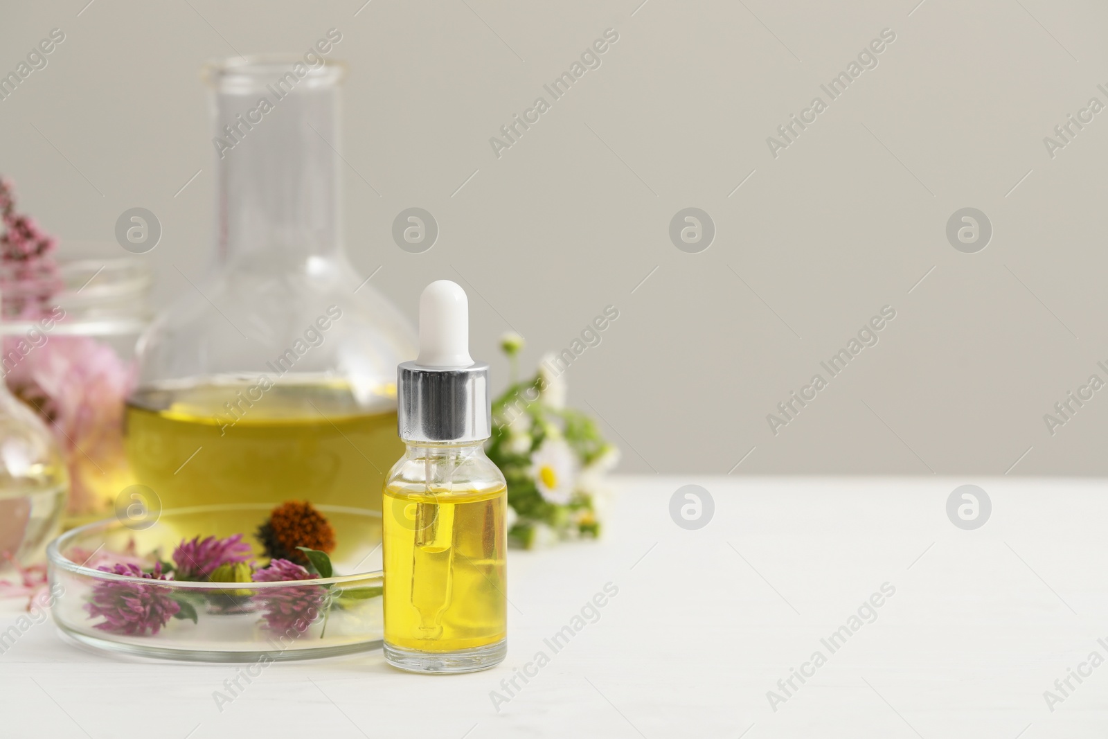 Photo of Cosmetic oil, laboratory dishware and flowers on white table, space for text