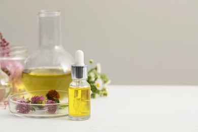 Cosmetic oil, laboratory dishware and flowers on white table, space for text