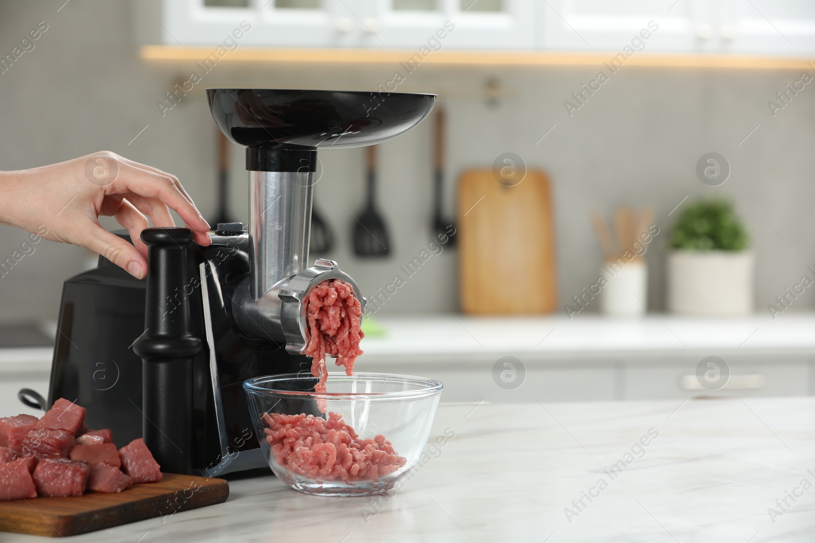 Photo of Woman making beef mince with electric meat grinder at white table in kitchen, closeup. Space for text