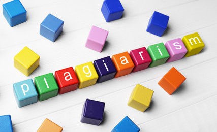 Photo of Colorful cubes with word Plagiarism on white wooden table, above view