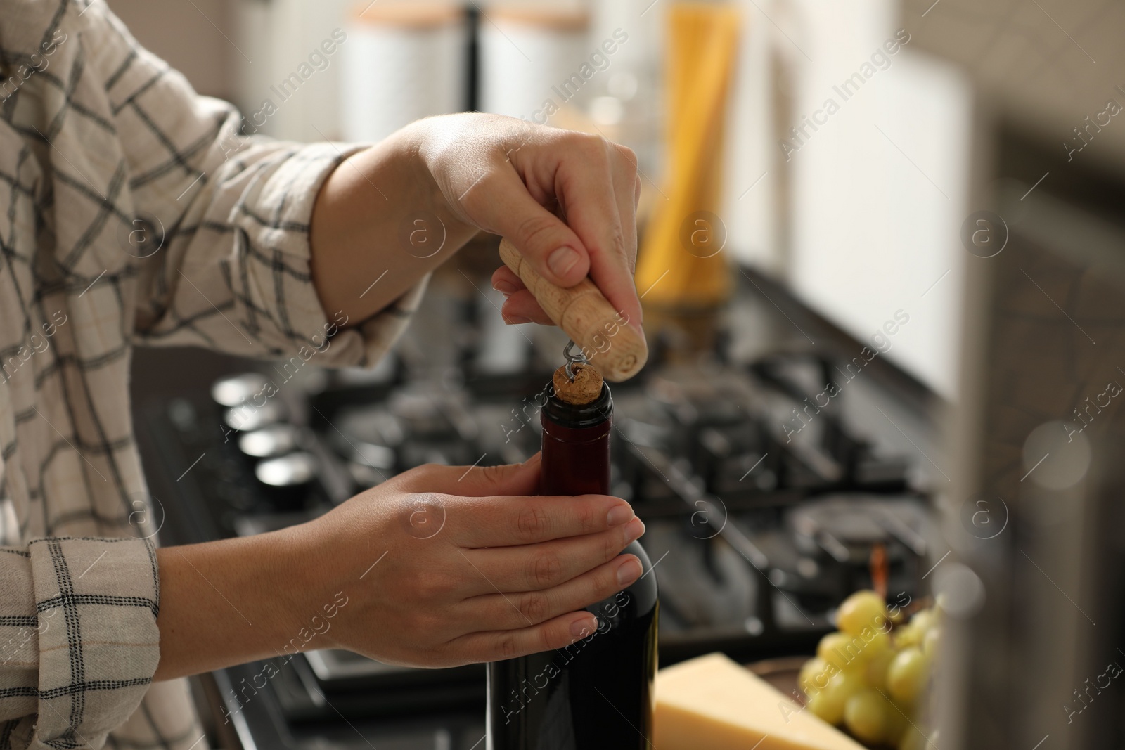 Photo of Woman opening wine bottle with corkscrew at countertop indoors, closeup