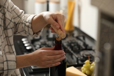 Woman opening wine bottle with corkscrew at countertop indoors, closeup